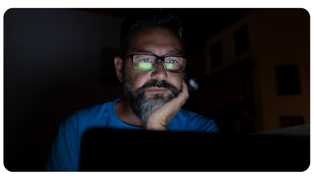 Man looking at a computer screen sitting in the dark