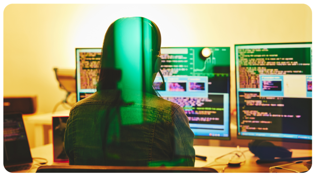 Person sitting in front of multiple screens with code.