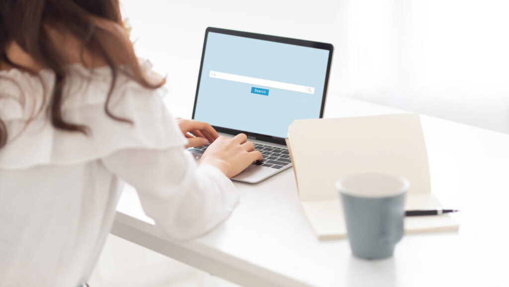 person in white at a desk using a laptop to search