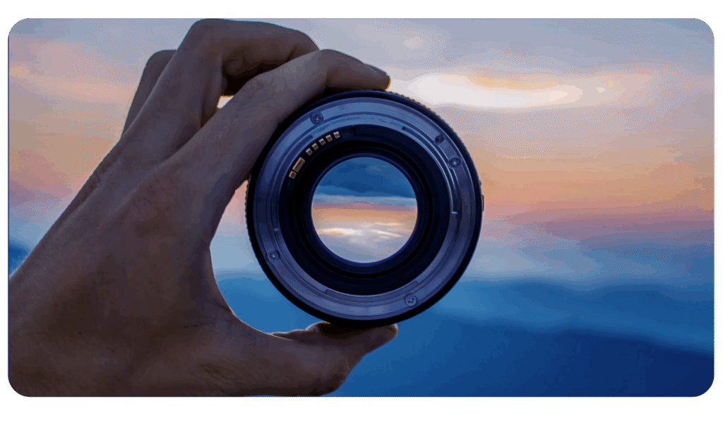 view of the ocean sunset through a person holding a camera lens.
