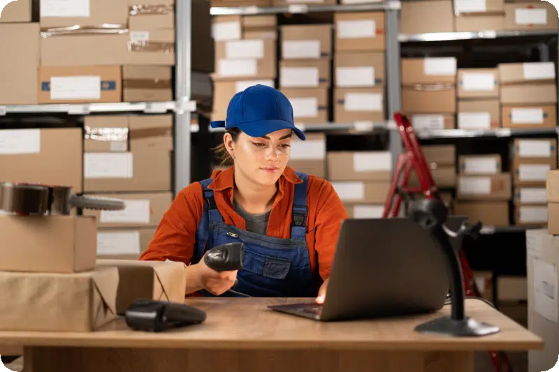 A young woman in a warehouse working with a laptop uses a barcode scanner enters data into the program